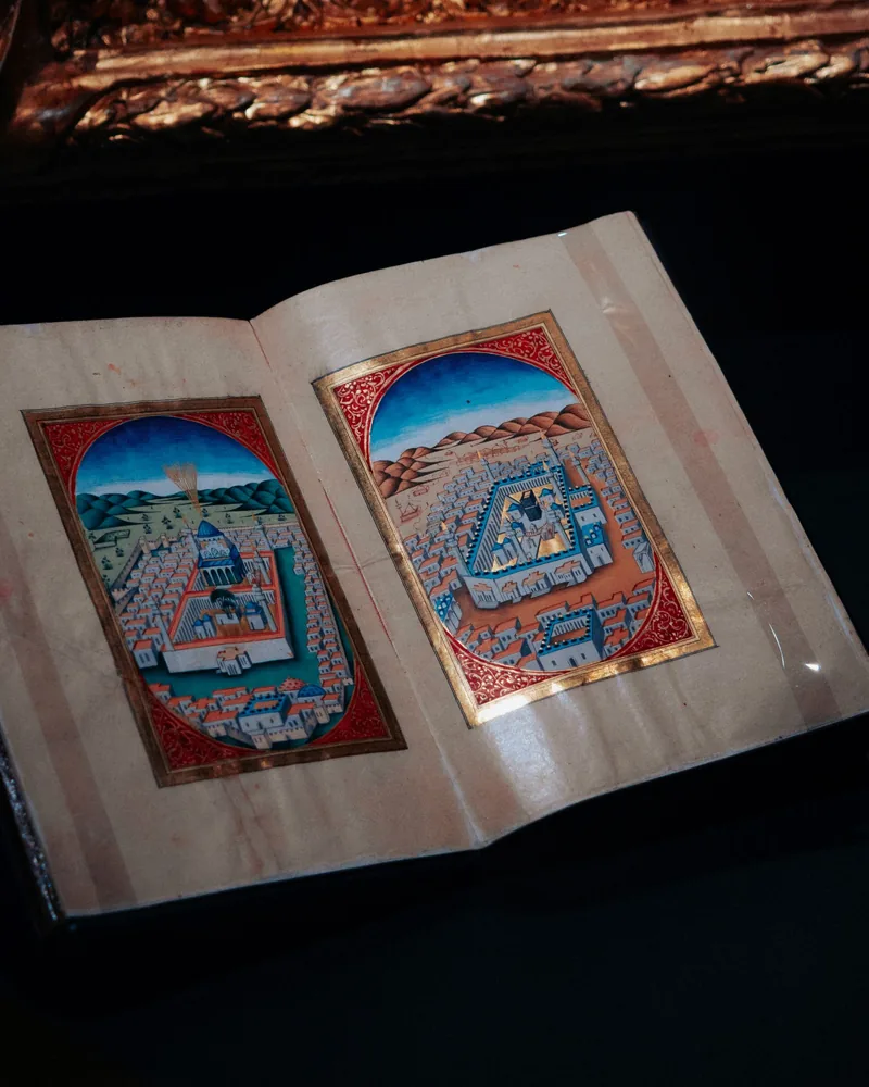 Manuscrito antiguo abierto con dos miniaturas enmarcadas en rojo y oro sobre papel envejecido